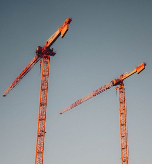 Why VTAR Two red tower cranes stand tall against a clear sky, symbolizing urban development.