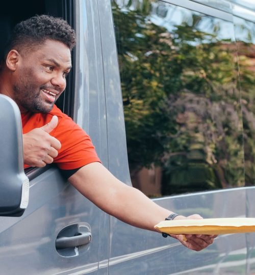 Why VTAR A delivery driver in a red shirt gives a thumbs up while handing a parcel from a van.